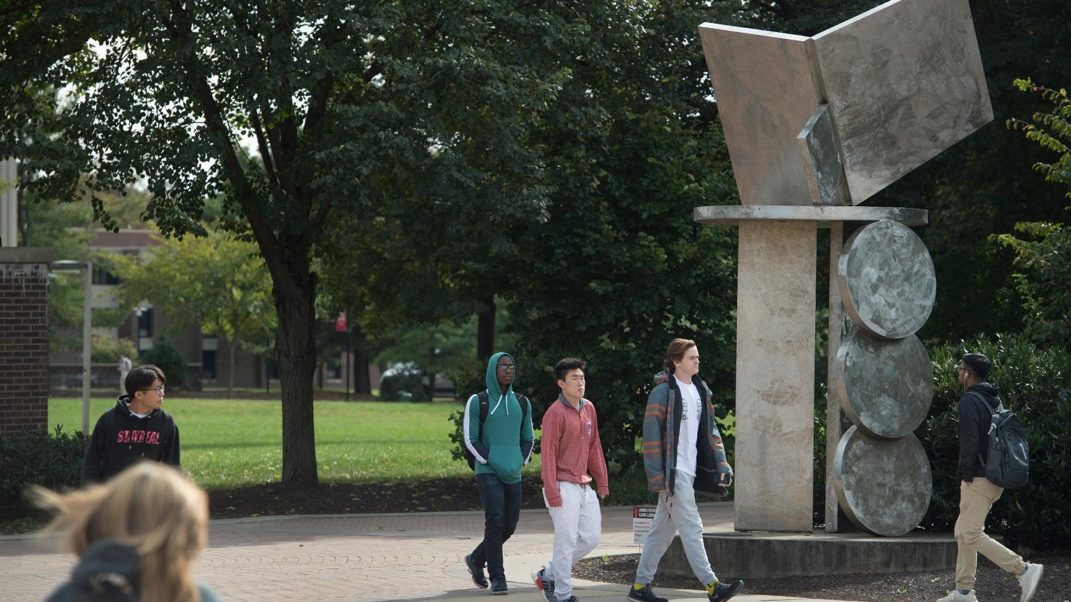 Students walk by Education is an Open Book sculpture on Livingston Campus