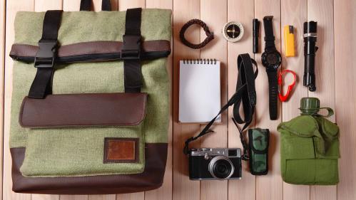 bird's eye view of canvas bag, notepad, camera, flashlight, water bottle, and a watch on a table