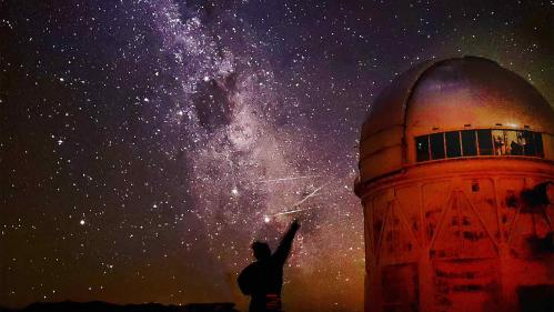 Person silhouetted against the sky with stars above and an observatory to the right