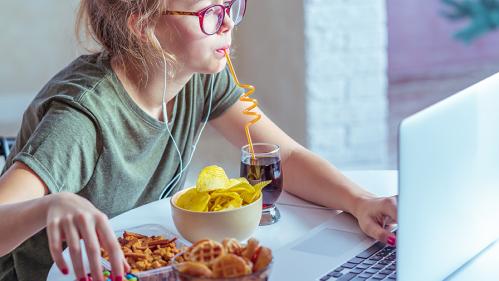 Young woman sitting in front of laptop with junk food arrayed before her