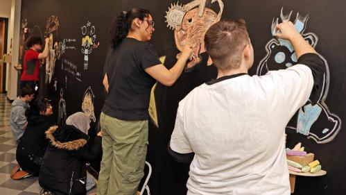 Students (from furthest left to right) Preston Romanienko, Andrew Hargy, Yumna Enver, Aman Kashmiri, Stayshey Sagastume-Castillo and Robin Mager draw on a collaborative chalkboard wall at the Mason Gross School of Arts on Monday.