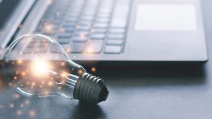 An illuminated lightbulb lies next to an open laptop