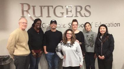 Smiling group of students standing in front of wall with Rutgers Graduate School of Education logo