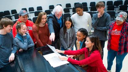 professor read sheet music while students stand around piano during byrne seminar