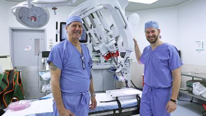 Rutgers Health surgeons wearing blue scrubs stand with a surgical robot in an operating room