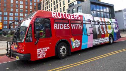 A scarlet red Rutgers campus bus with wrap celebrating Pride Month