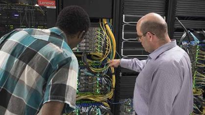 Two people examining machine wiring.