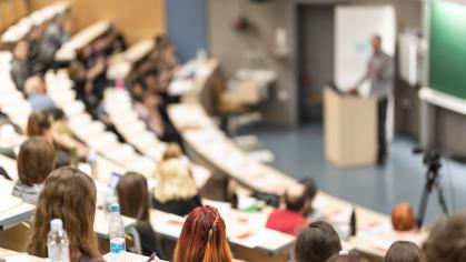 A professor stands at a podium surrounded by students in a lecture hall