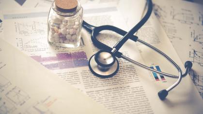 A stethoscope and bottle of medication sits on a desk covered in research articles