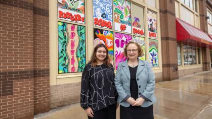 Art & Design student Ria Monga standing in front of a 10-panel vinyl installation in the first-floor windows of the Rutgers School of Social Work building in New Brunswick