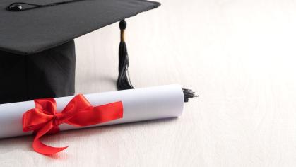 A black graduation and a degree document, rolled and secured with red ribbon