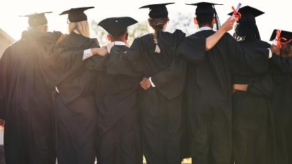 An image of a group of graduates in caps & gowns hugging from behind