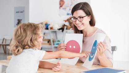 A therapist working with a child asking them to identify their emotions by pointing to a happy or sad face on a piece of paper