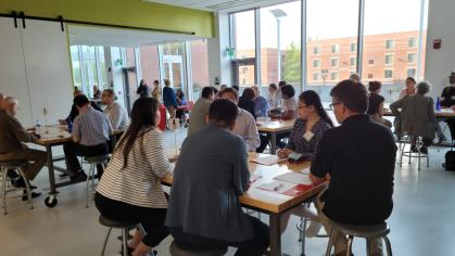 People seated at tables in a bright, modern room with large windows, engaged in conversation during a professional networking event.