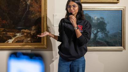 A smartphone records Rutgers sophomore Aditi Sandhir discuss a painting on the wall at the Zimmerli Art Museum.