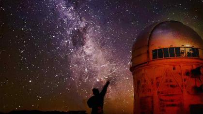 Person silhouetted against the sky with stars above and an observatory to the right