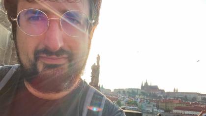Ilya Slavutskiy stands near Charles Bridge. Behind him is a view of the Prague Castle complex and St. Vitus Cathedral.