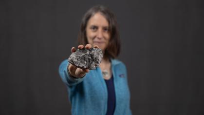 Woman in light blue sweater holds up breccia, a type of rock found on the Moon.