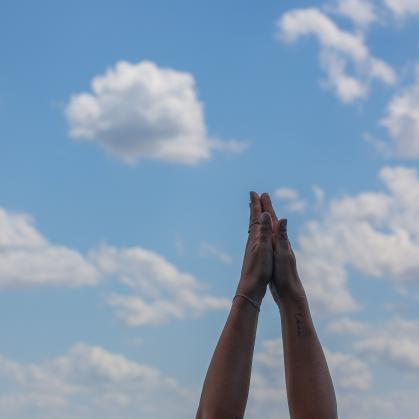 A person doing yoga holds their hands together against a blue sky background