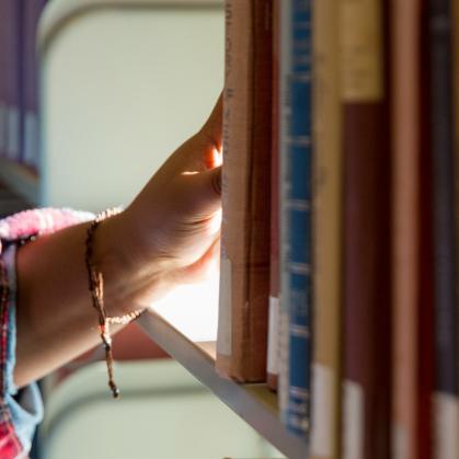 A student's hand reaching for a book on a shelf in Alexander Library