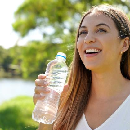 A woman stands by a lake on a sunny day holding a water bottle