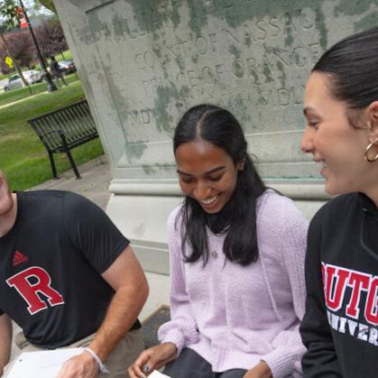 Three students seated outside in front of a statue