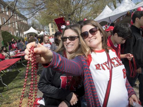 Two alumni wearing Rutgers colors and holding red beads march in the parade at Rutgers Day