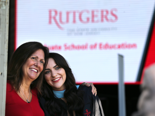 A graduate posing for a picture with their parent at a Graduate School of Education ceremony