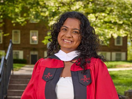 Anjali Vijan standing in front of the Old Queens gate holding her graduation cap.