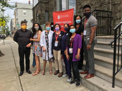 Zelia DeSouza, a parishioner at the Luso-Brazilian Seventh-day Adventist Church and recently retired Rutgers Community Outreach Coordinator (in white coat) with her family are pictured with the Stonsby Vaccination Clinic team to hosting a pop-up vaccination clinic (from left to right):  Noa'a Shimoni, Devin McNair, Marissa Smith, Donnell Pierre and student volunteer Rutvi Upadhyay (bottom right).