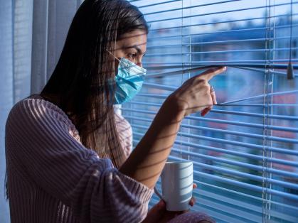 women in mask looking out window