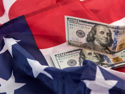 A portion of a flag is seen with Ben Franklin's - $100 bills scattered.