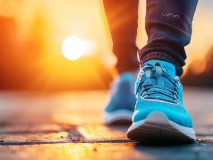 A view of a person's sneakers and shins. The person is walking and the sun is rising behind the person