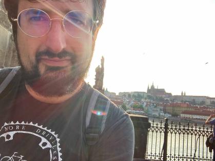 Ilya Slavutskiy stands near Charles Bridge. Behind him is a view of the Prague Castle complex and St. Vitus Cathedral.