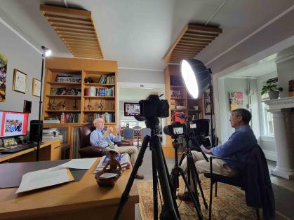 Two men in office, one interviewing the other with video camera