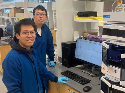 Two men stand in a laboratory before a chemistry research machine.