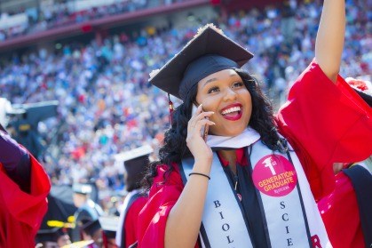 A jubilant graduate with a sticker reading "First Generation Student" on her graduation gown