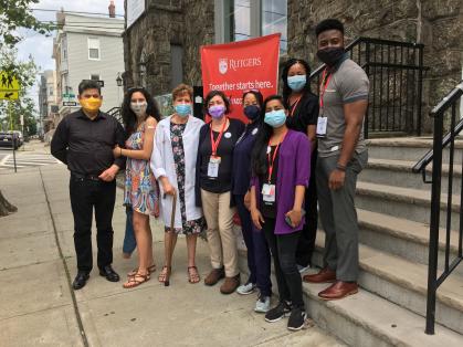 Zelia DeSouza, a parishioner at the Luso-Brazilian Seventh-day Adventist Church and recently retired Rutgers Community Outreach Coordinator (in white coat) with her family are pictured with the Stonsby Vaccination Clinic team to hosting a pop-up vaccination clinic (from left to right):  Noa'a Shimoni, Devin McNair, Marissa Smith, Donnell Pierre and student volunteer Rutvi Upadhyay (bottom right).