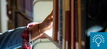 A student's hand reaching for a book on a shelf in Alexander Library