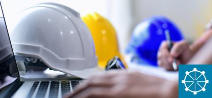 A hand types on a keyboard with white blue and yellow hard hats in the background