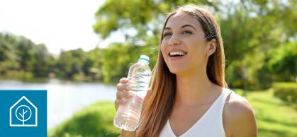 A woman stands by a lake on a sunny day holding a water bottle
