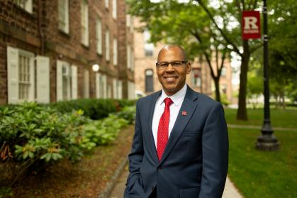 Photo of Provost Geary in front of a Rutgers building and Rutgers flag post
