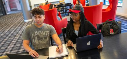 two students seated at a table in front of two lap tops