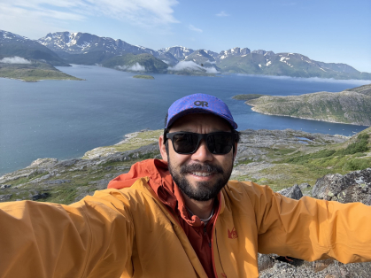 A man at the top of a mountain in front of a landscape of a body of water