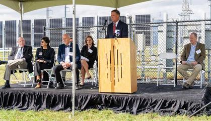 Man speaking at podium with solar cells behind him.