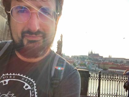 Ilya Slavutskiy stands near Charles Bridge. Behind him is a view of the Prague Castle complex and St. Vitus Cathedral.