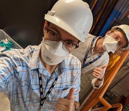 Two men wearing construction helmets in an experimental machine.