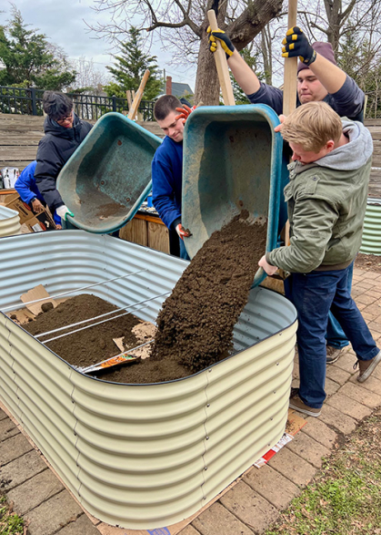 Two students pour dirt into a vegetable bed they've created