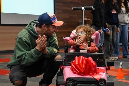Kevin Groff with his daughter Zora, who is riding a pink car toy that Rutgers students redesigned for her.