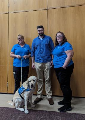 Three staff members and a service dog from Canine Companions pose for a photo during Disability Awareness Month at Rutgers